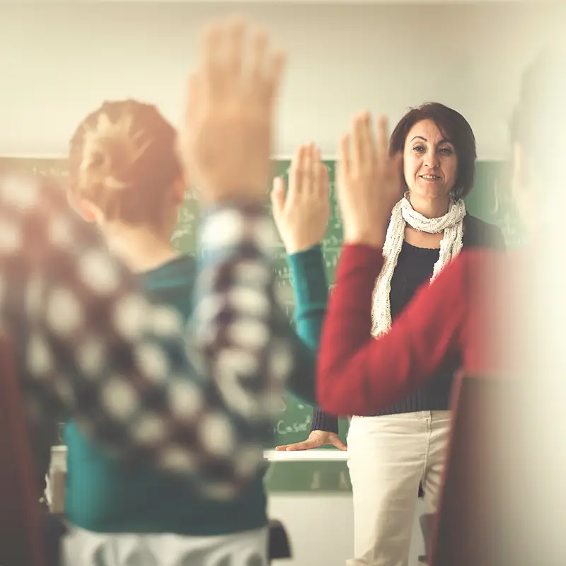 A teacher in a classroom with students raising their hands