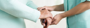 Close up of caregiver holding hand of elderly person with cane.