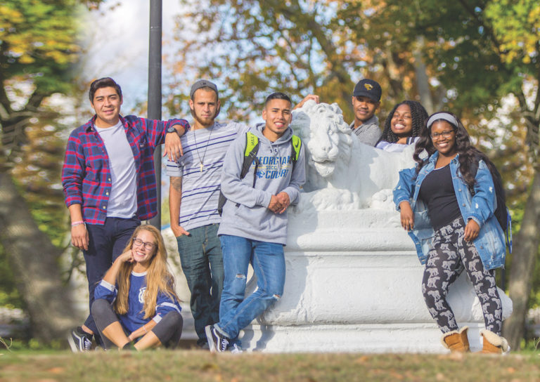 A group of students standing against a lion statue in campus