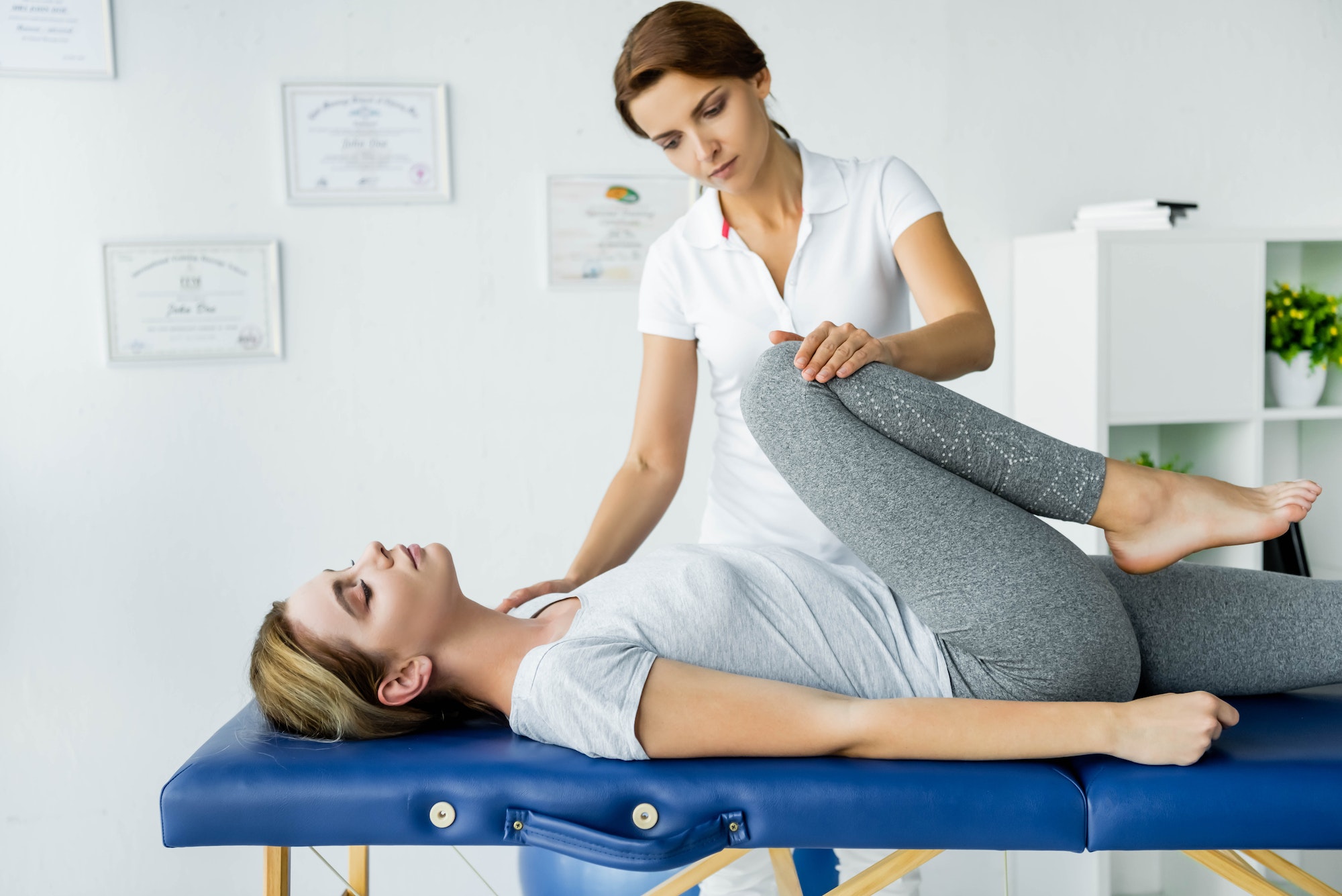 chiropractor touching leg of attractive patient in grey t-shirt