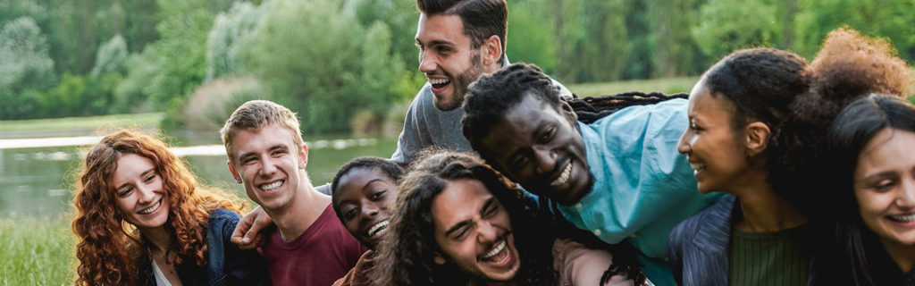 Multiethnic happy group of people having fun outdoor by the lake - Focus on blond man face