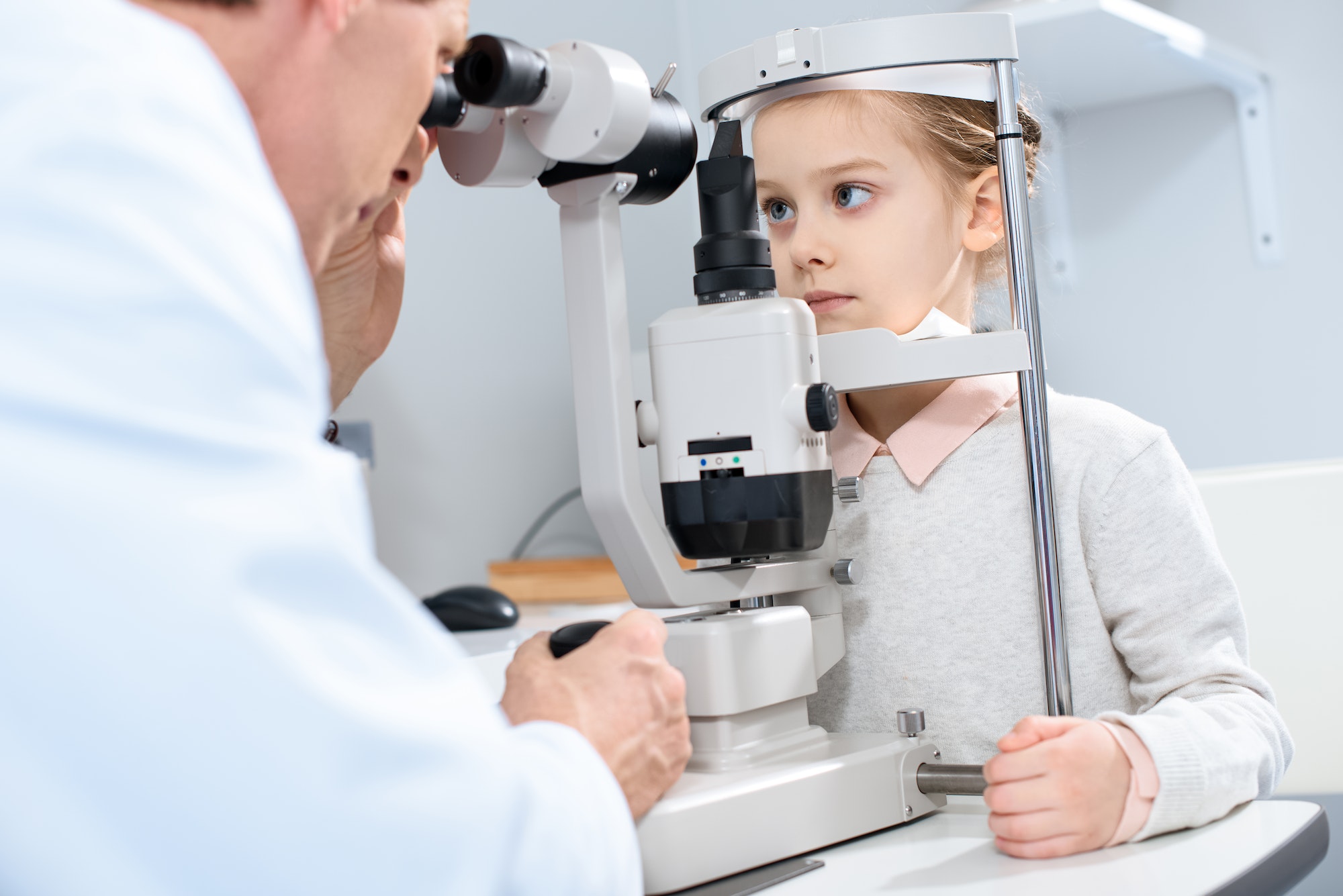 ophthalmologist examining pre-adolescent child vision with slit lamp in clinic